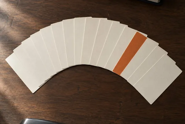 Ein Fächer leerer Karten auf einem dunklen Schreibtisch, eine davon orange